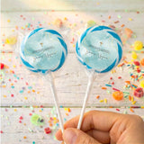 Two blue cross lollipops in clear wrappers on sticks, held in hand