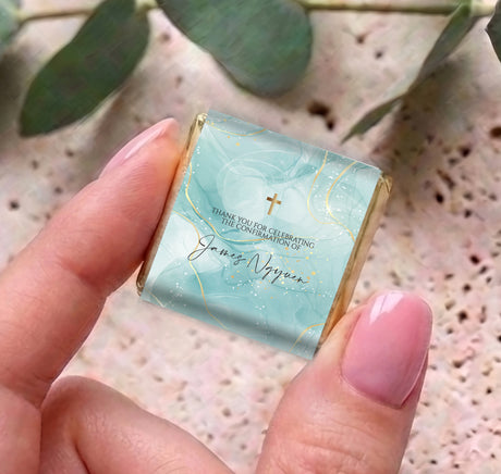 Mini personalized chocolate box with teal wrap, gold cross, held in hand