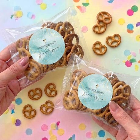 Personalised pretzel bag with light-blue label and gold cross, filled with brown pretzels