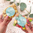 Personalised popcorn bag with blue round cross sticker, held in hands, clear crinkle wrap