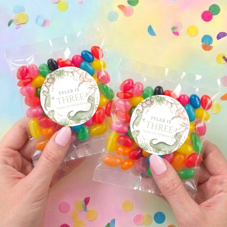 Two dinosaur jelly bean bags held, each with round 'TYLER IS THREE' label and candy