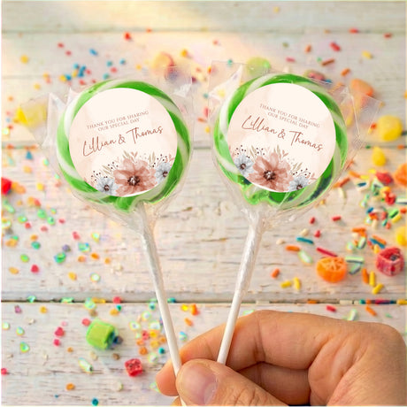 Personalised wedding lollipops with green-edged floral thank-you labels, two wrapped sticks