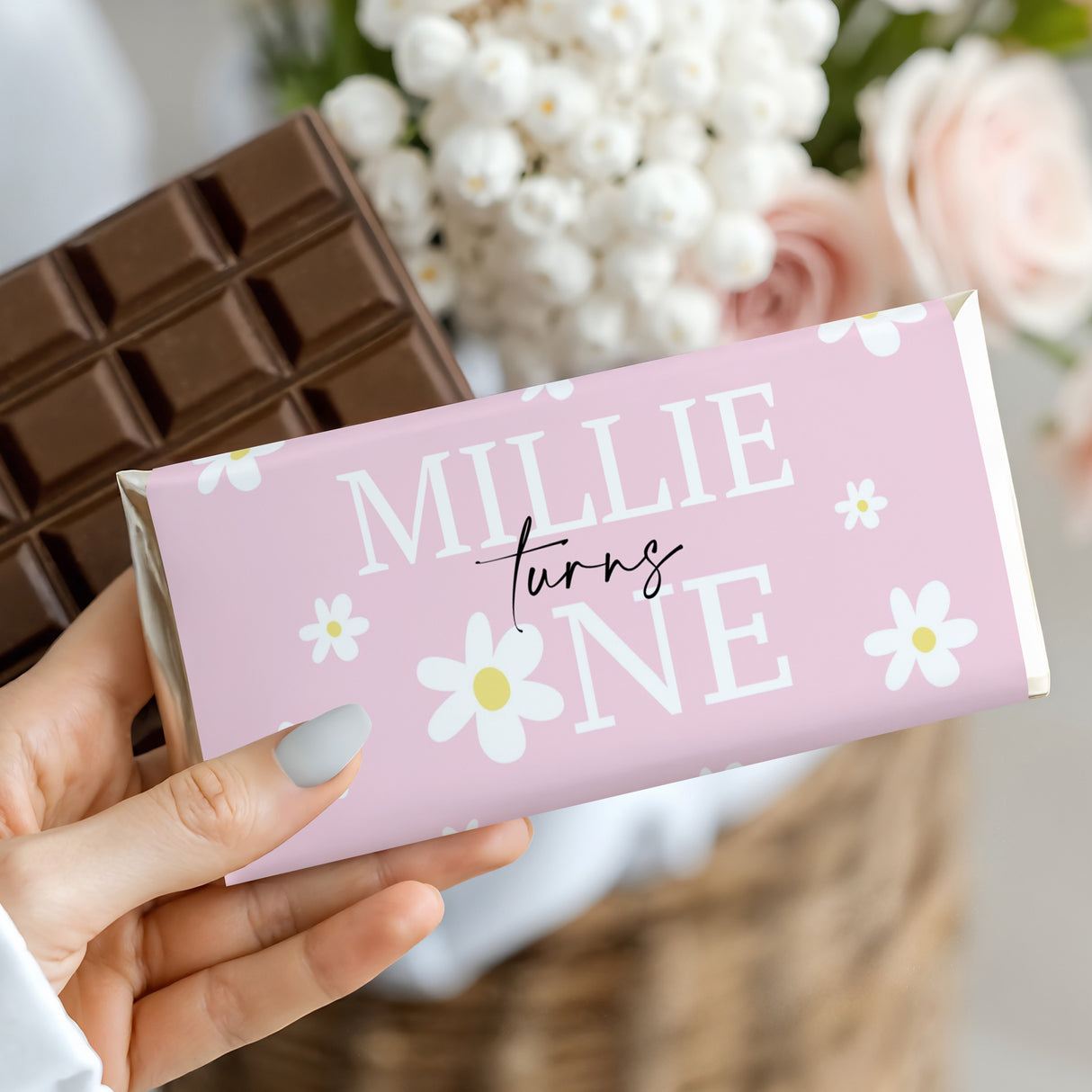Pink birthday chocolate bar wrapper: 'MILLIE turns ONE' with daisy icons