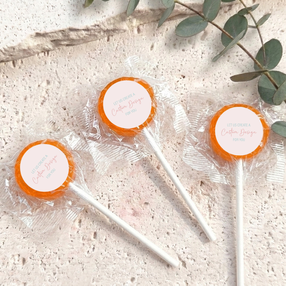 Mini lollipops with orange lollipop tops, wrapped in clear plastic on white sticks.
