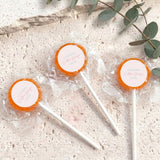 Mini lollipops with orange lollipop tops, wrapped in clear plastic on white sticks.