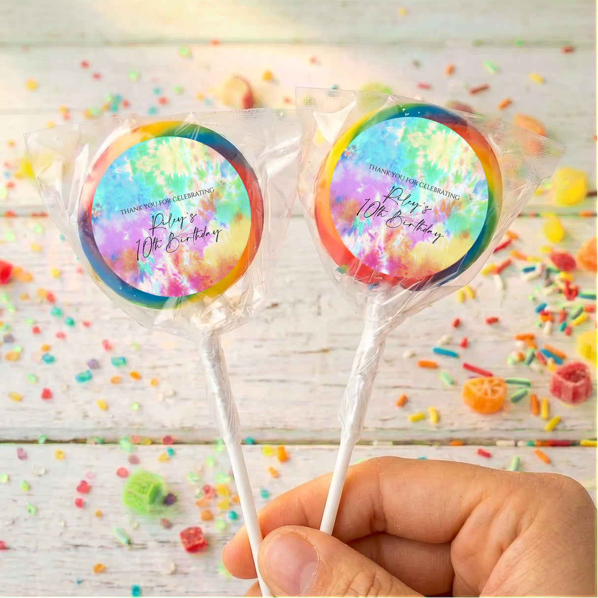 Two tie dye birthday lollipops in clear wrappers, multicolor rainbow swirls