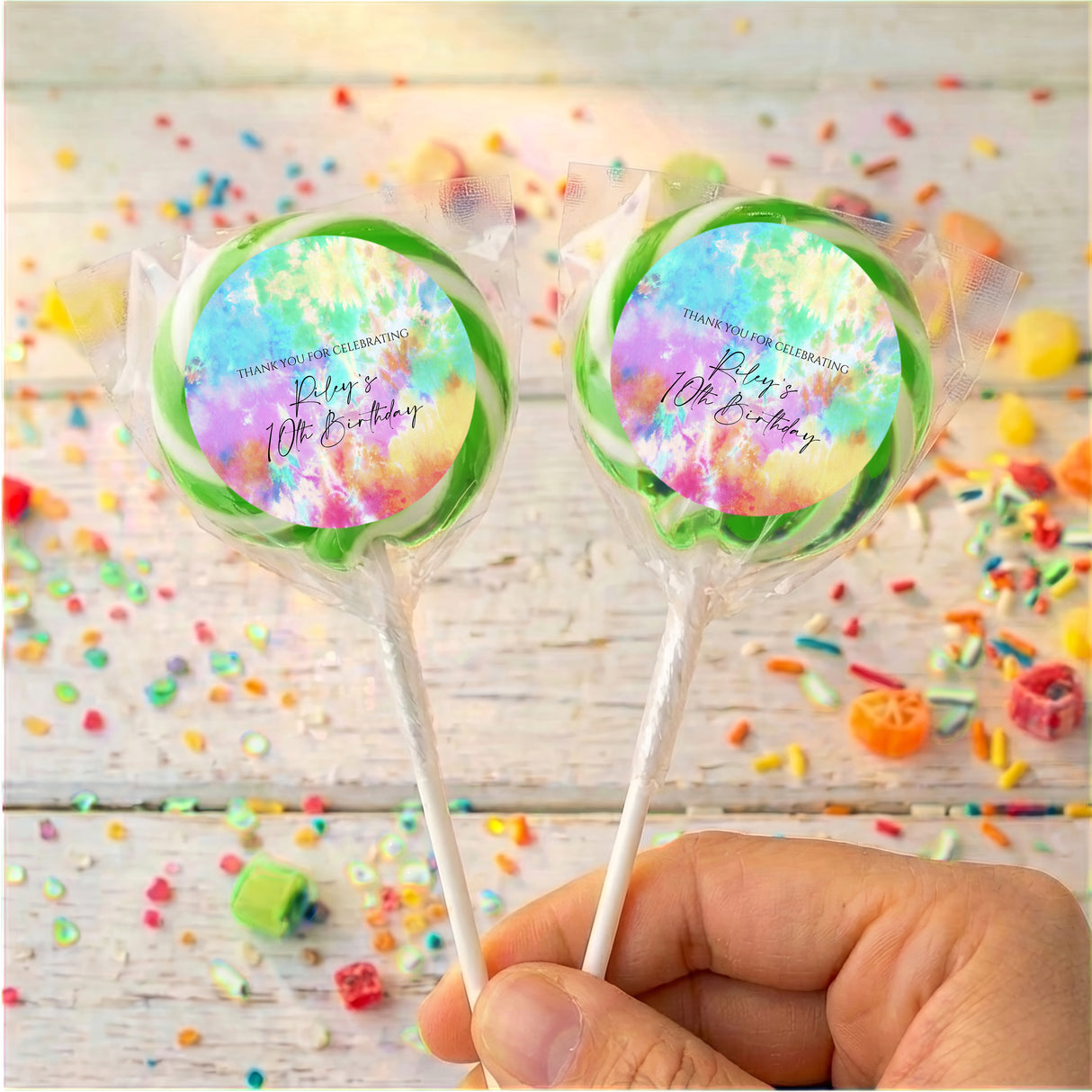 Two tie dye birthday lollipops in clear wrappers, green and rainbow pastel swirls