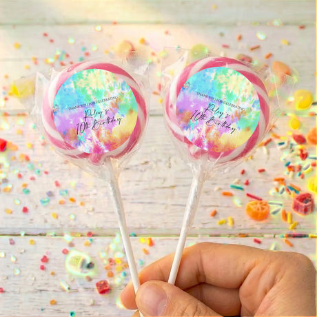 Two tie dye birthday lollipops in clear wrappers, printed message, held by hand