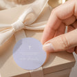 Round christening label with lavender cross and name text, tied with satin ribbon