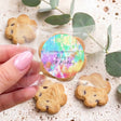 Hand holding tie-dye birthday cookie topper on chocolate chip cookie; other cookies nearby