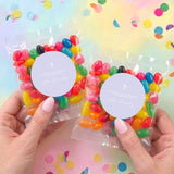 Two christening jelly bean bags held in hands, cross on lavender round labels