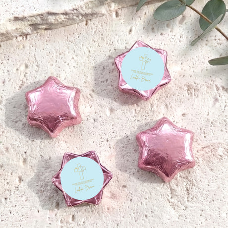 Foil-covered chocolate stars in pink with printed cross on white labels.