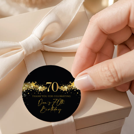 Round black 70th birthday label with gold stars and “70” text