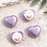 Purple foil-covered chocolate hearts with floral name labels on textured surface