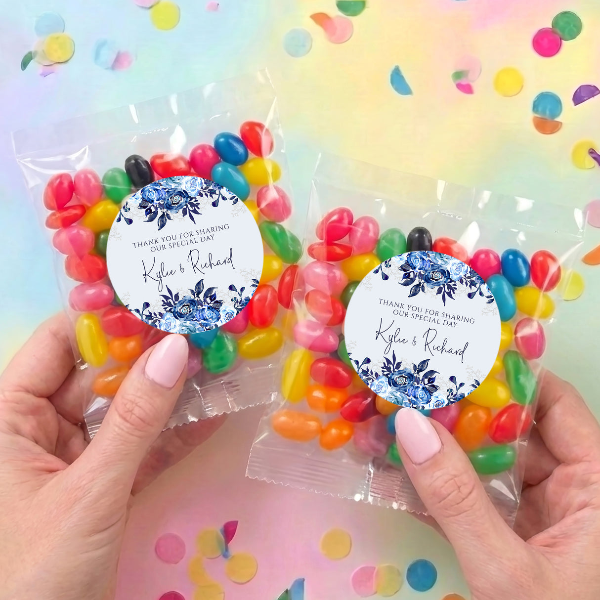 Two hands holding personalized jelly bean bags with blue floral round labels