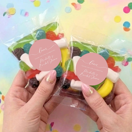 Two personalised lolly bags with clear wrappers and round pink thank-you labels, held by hands
