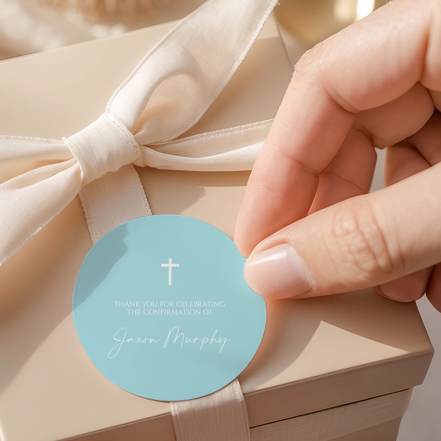 Pastel blue round confirmation label with white cross and text, held by hand