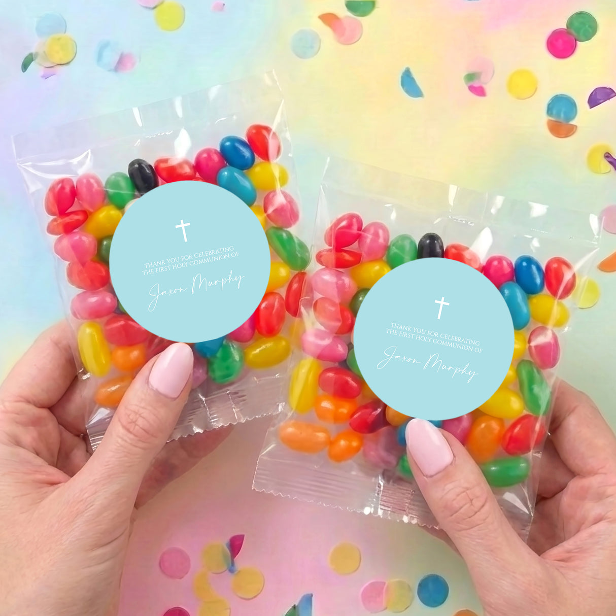 Two pastel blue cross jelly bean bags held in hands, clear pouches with assorted beans