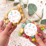 Personalised baby shower popcorn bag with butterfly round label, held in hands, clear wrap