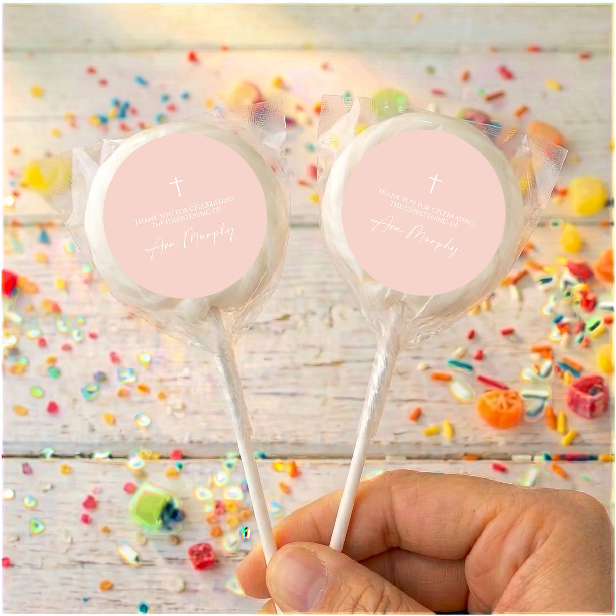 Personalised cross lollipops with clear white wrap, round personalised label, held in hand