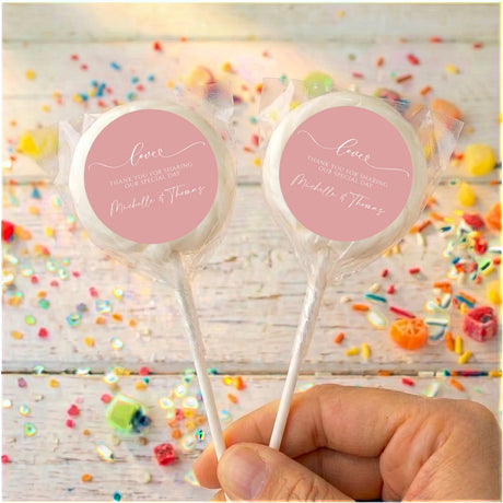 Personalised dusty pink lollipops with clear wrappers, round love labels, held in hand