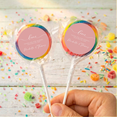 Personalised dusty pink lollipops with rainbow-edged wrappers, round love labels, held in hand