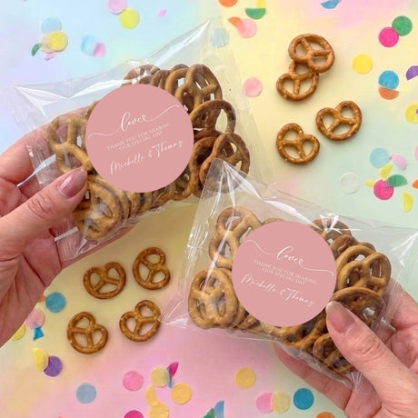 Personalised dusty pink pretzel favor bags with clear plastic packets and round name labels