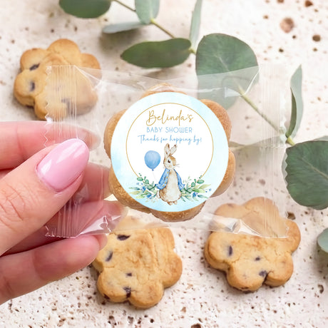 Hand holding round baby shower choc chip cookie with blue rabbit floral label