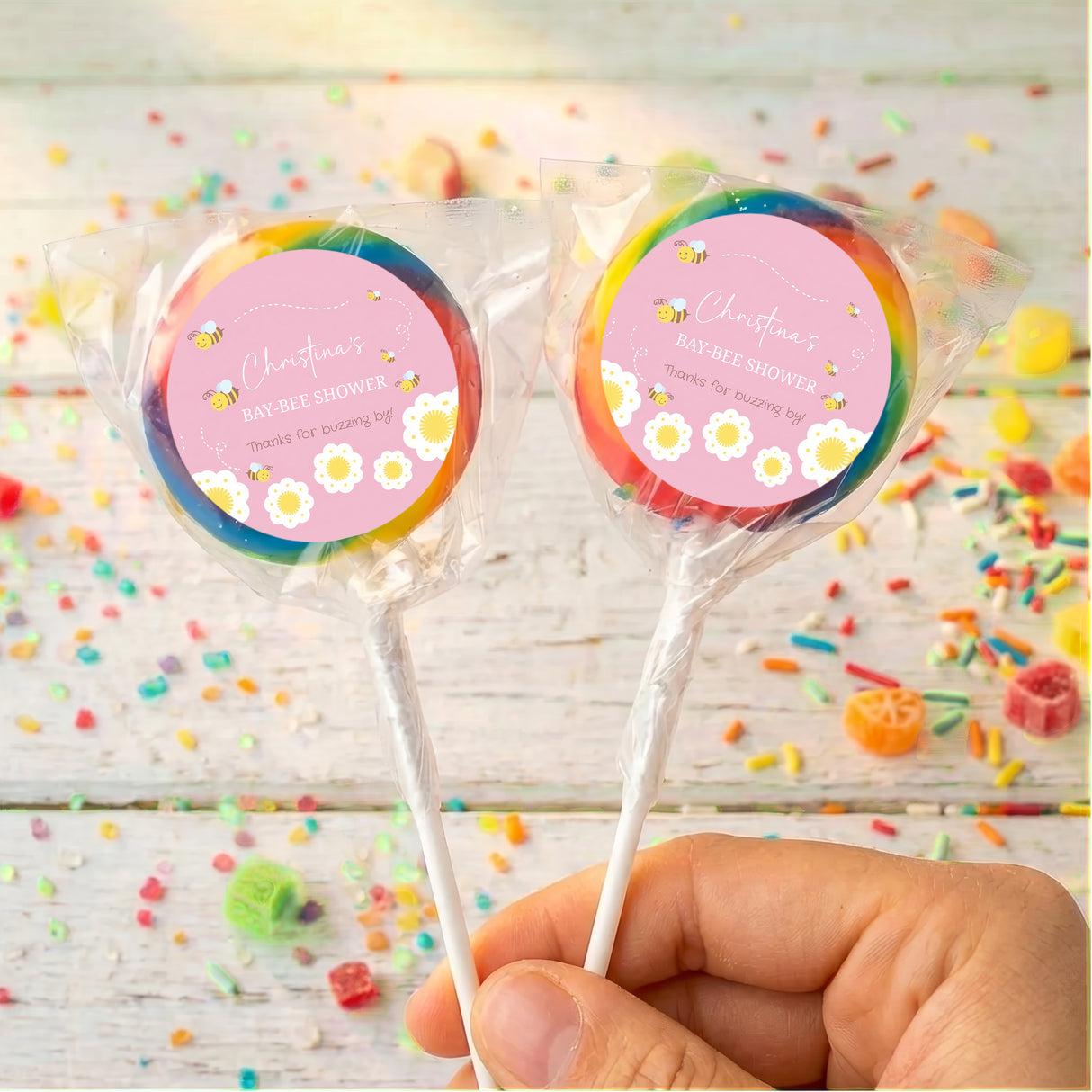 Bee-themed baby shower lollipops, two pops with rainbow outer wrappers and pink labels