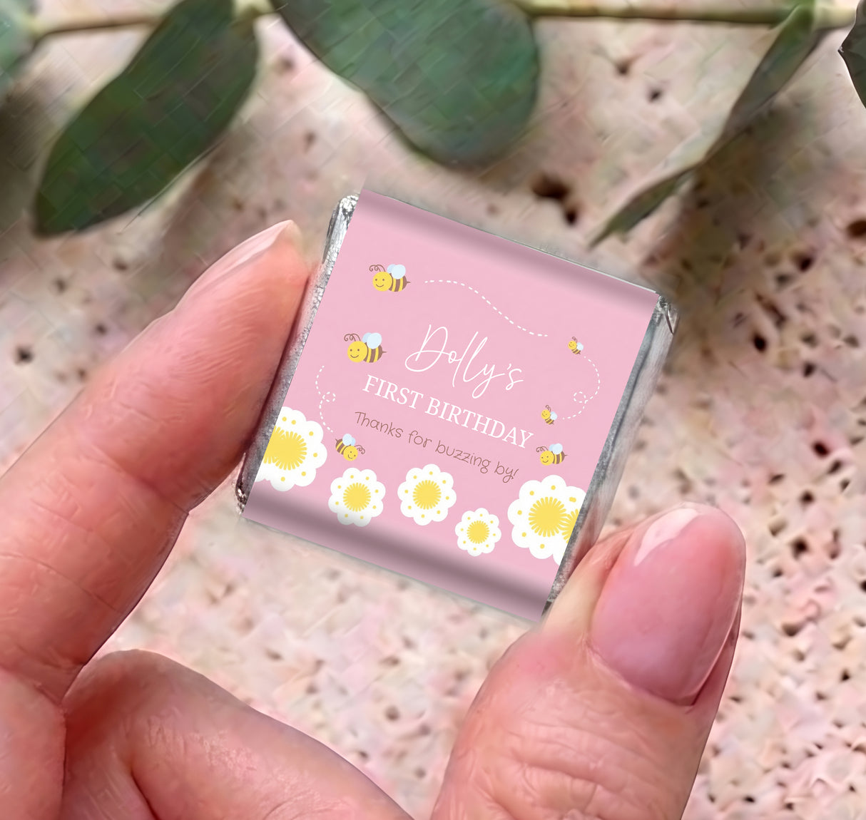 Pink mini chocolate box held in fingers, “Dolly’s First Birthday” bee flower design
