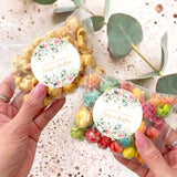 Transparent popcorn bag with pink floral thank-you label; pastel popcorn mix, held in hands