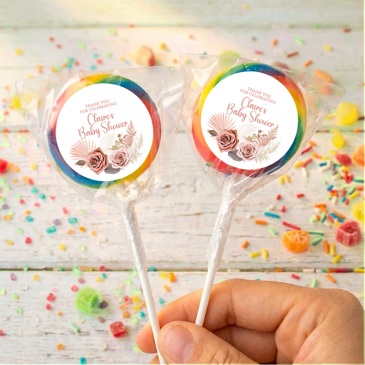 Personalised baby shower lollipops with rainbow floral round labels, held in hand