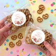 Two clear pretzel bags with brown pretzels and pink floral baby shower round labels