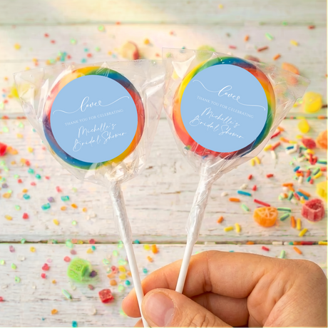 Bridal shower lollipops with blue personalized labels and rainbow candy swirls, held by hand