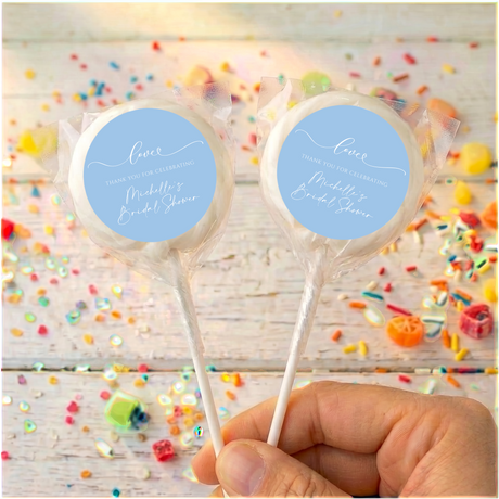 Bridal shower lollipops with blue personalized circle labels on white sticks, held by hand
