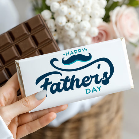 Hand holding Father's Day chocolate bar in white wrapper with 'Happy Father's Day' mustache