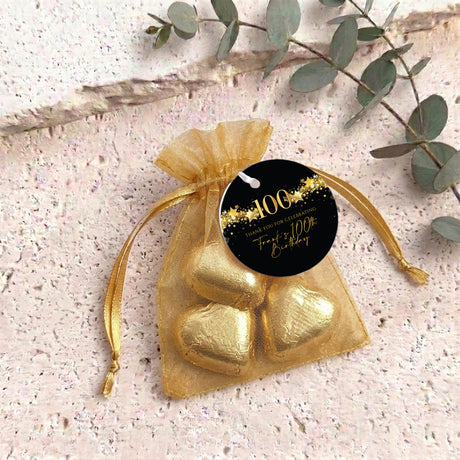 Gold organza treat bag with gold heart-shaped chocolates and gold 100th round tag