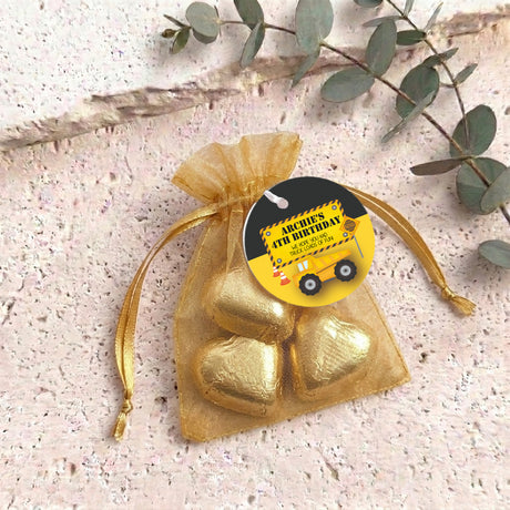 Gold organza gift bag with two gold heart-shaped chocolates and a black gift tag.