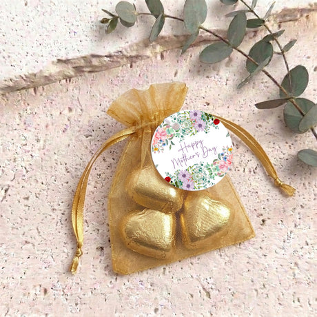 Gold organza gift pouch with drawstring, golden heart-shaped chocolates, floral “Happy Mother’s Day” tag