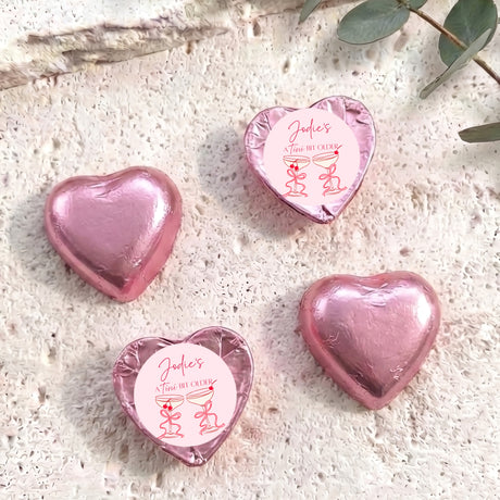Pink foil-covered chocolate heart candies with round label and red ribbon design