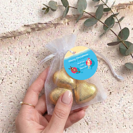 Gold metallic heart-shaped treat in clear organza drawstring bag held in hand with blue round tag