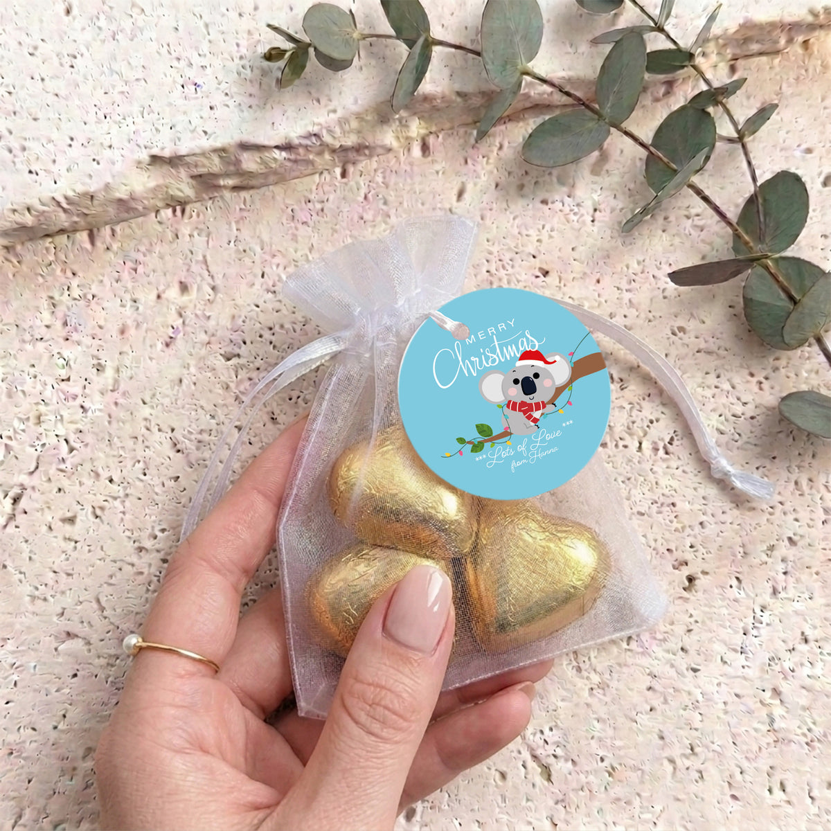 Gold heart chocolates in sheer white organza drawstring gift bag, held by hand with label