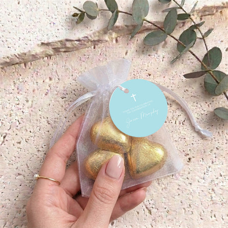 Translucent organza pouch with gold heart-shaped chocolates, held by hand, with cross tag.