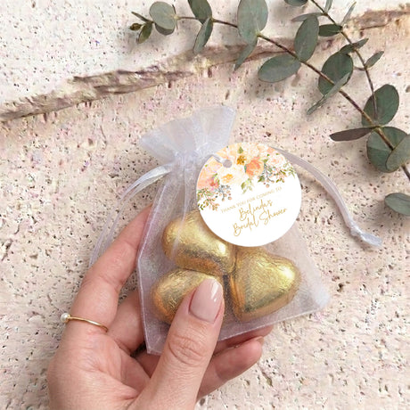 Bridal shower organza pouch in hand with gold heart chocolates and floral round label