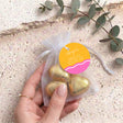 Gold organza favor bag with three chocolate heart pieces, held by a hand