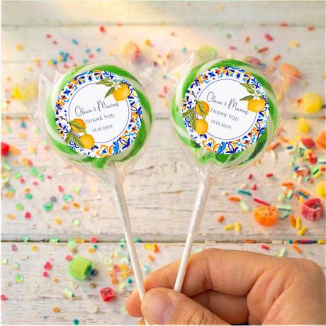 Hand holding two personalized wedding lollipops with blue border labels and small thank-you lines