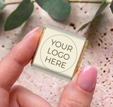 Mini personalized chocolates with cream wrapper and “YOUR LOGO HERE” label, held in hand