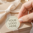Round personalised printed label with “YOUR LOGO HERE” text, held by hand