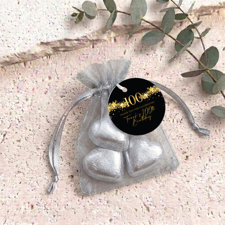 Silver organza treat bag with silver heart-shaped chocolates and gold 100th round tag