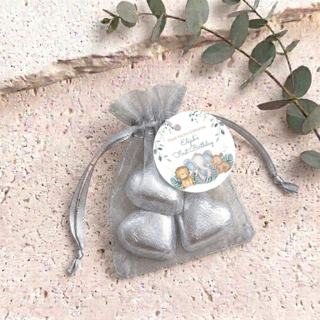 Silver organza baby shower bag tied with ribbon, filled with gold heart chocolate treats